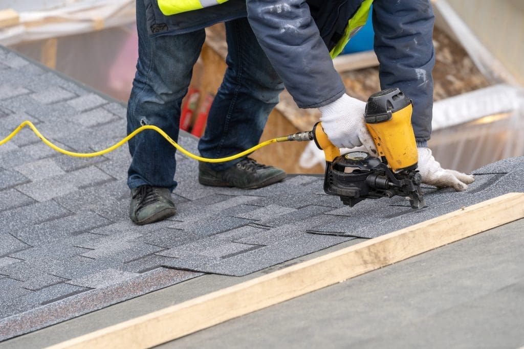 roofing contractor installing asphalt shingles with nail gun