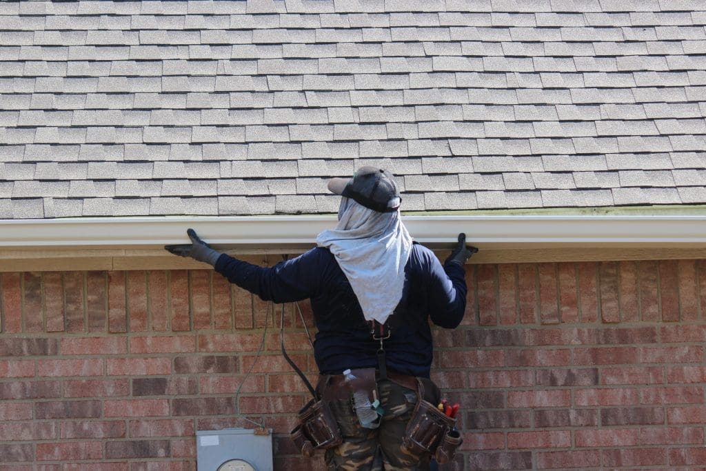 man installing gutter system on the side of a 1 story house