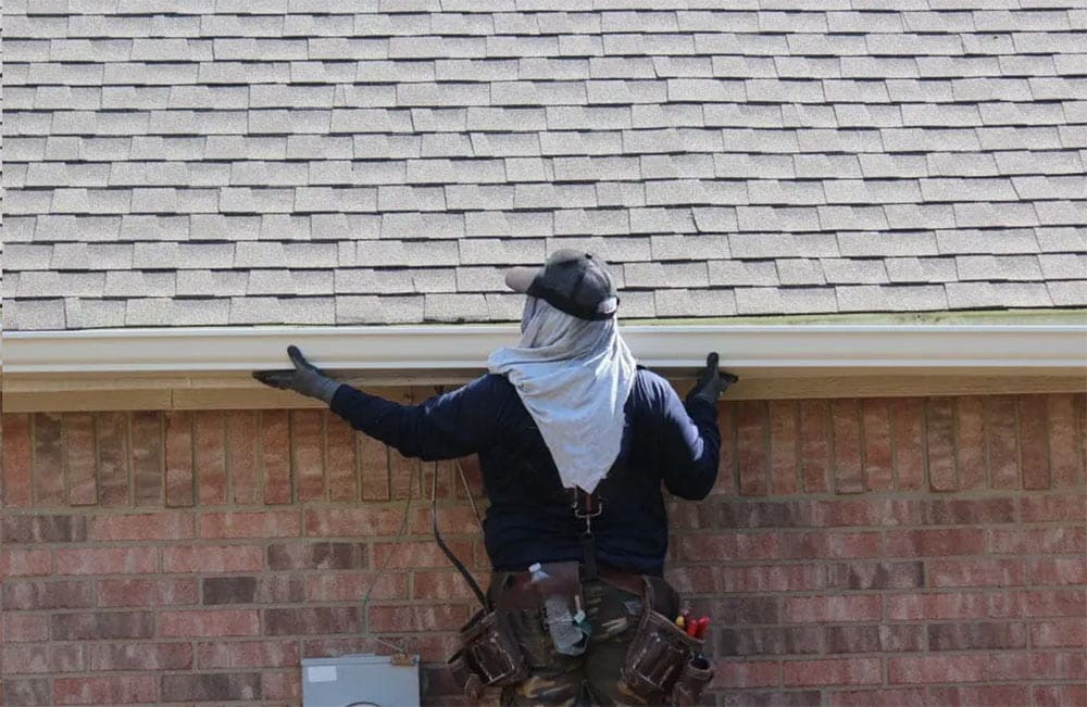 man installing gutter system on the side of a 1 story house