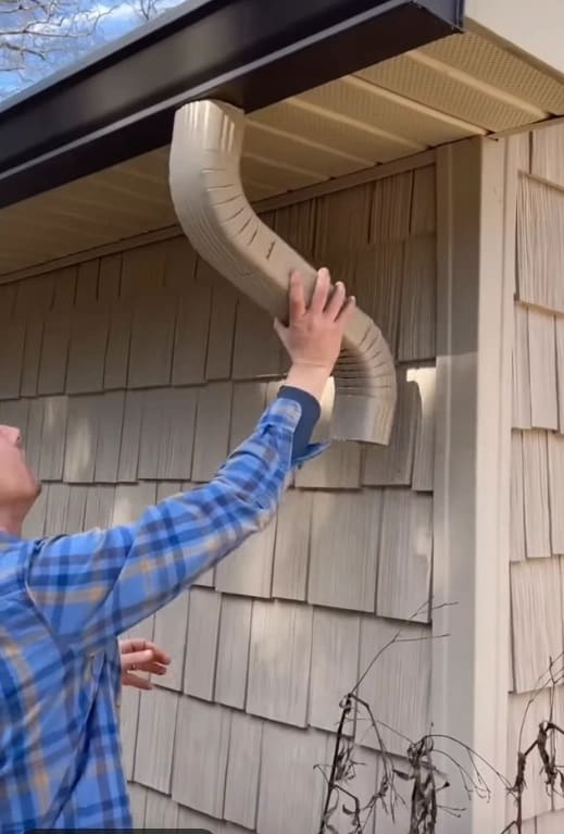 Technician from a roofing company in Loudon County installing a curved downspout to improve home gutter drainage